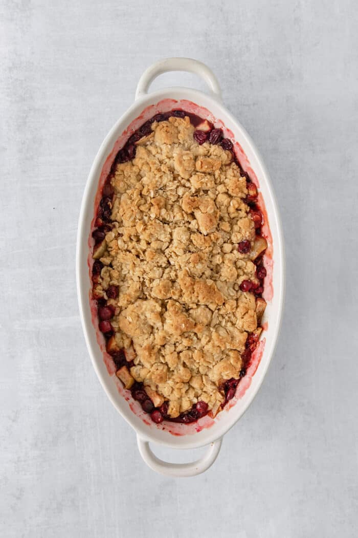 This Cranberry Apple Crisp features fresh, sweet-tart cranberries and apples, plus a crispy, buttery oat topping. A white oval baking dish holds a baked cranberry apple crisp.