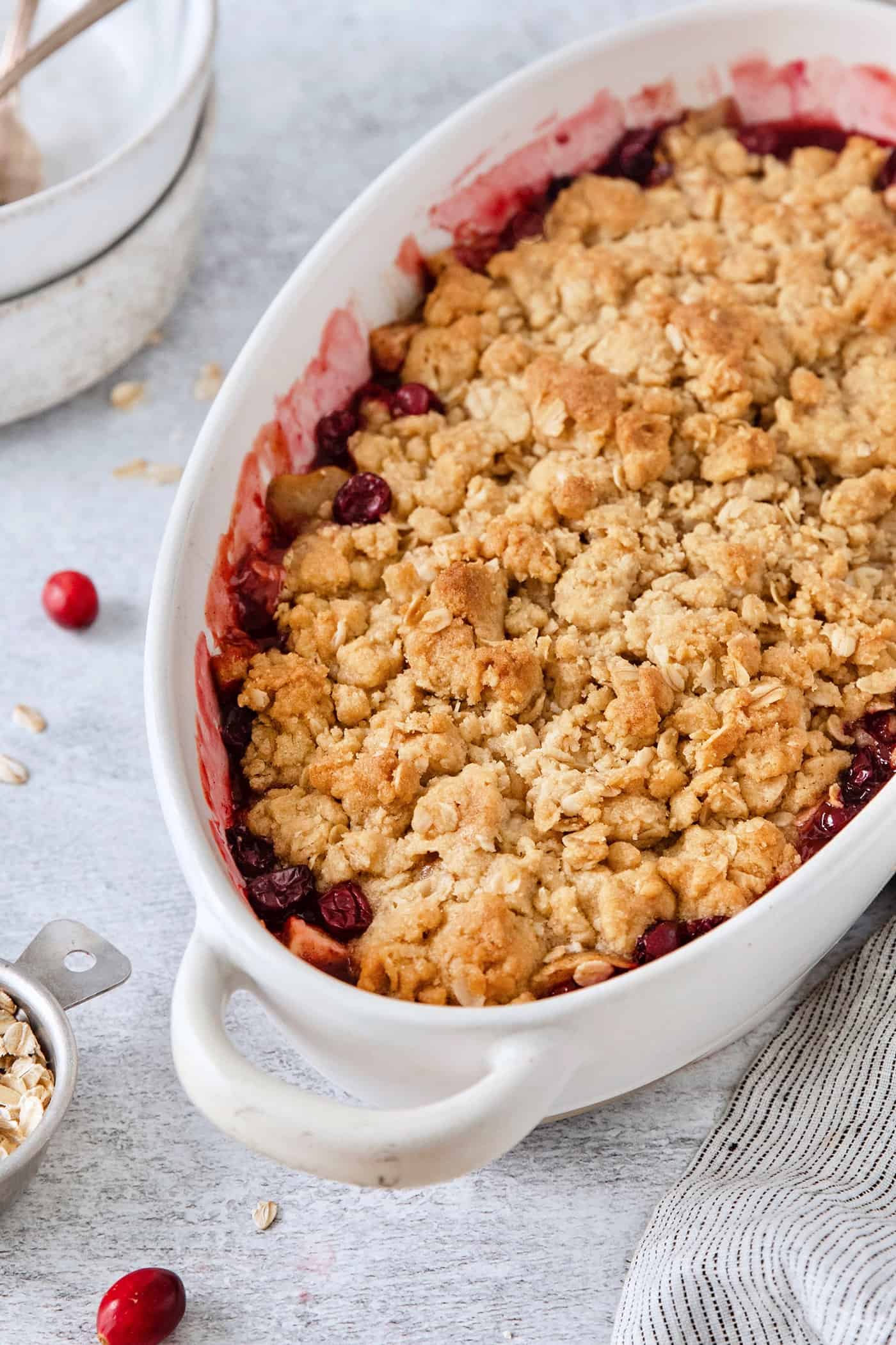This Cranberry Apple Crisp features fresh, sweet-tart cranberries and apples, plus a crispy, buttery oat topping. A white oval baking dish holds a baked cranberry apple crisp.