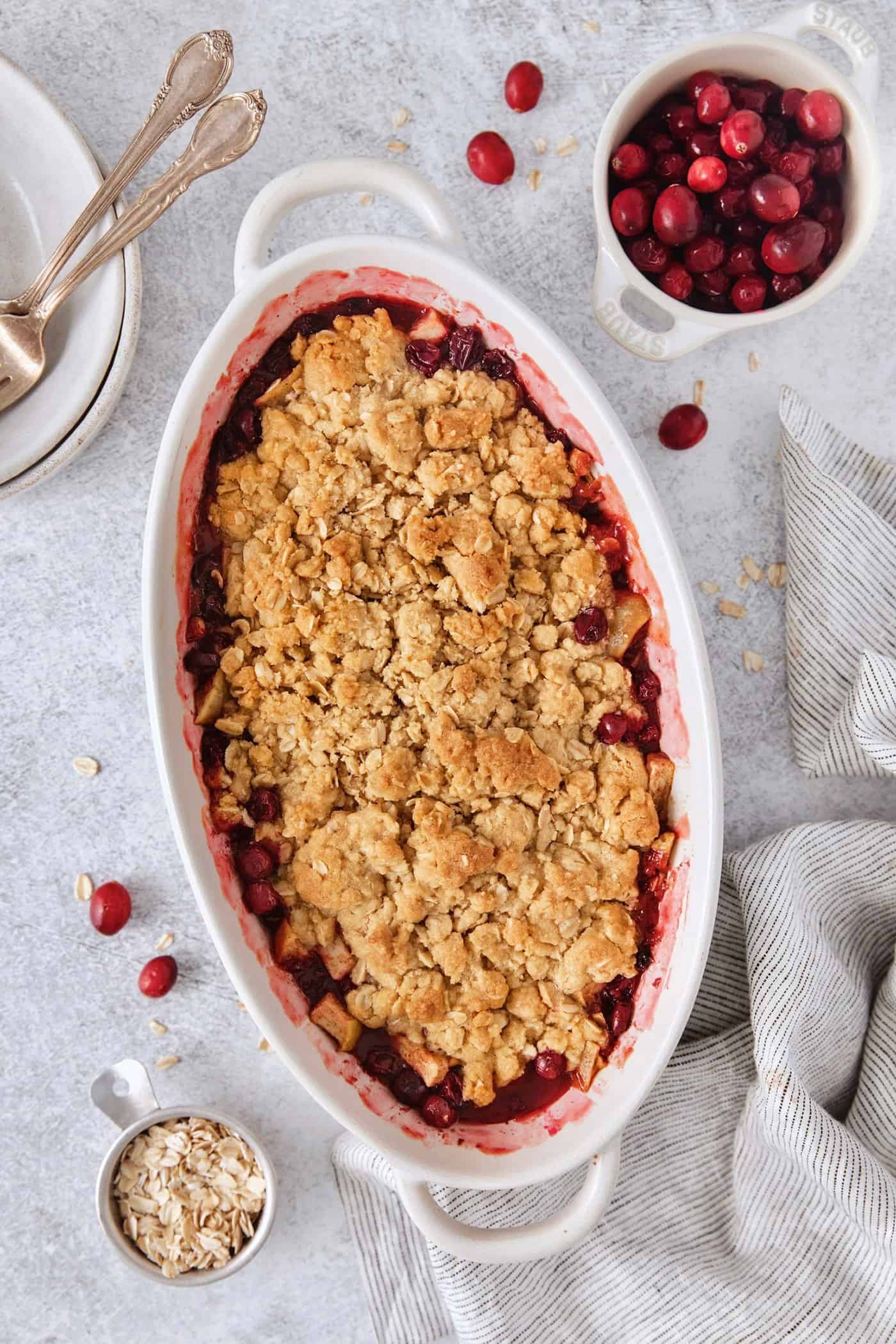 This Cranberry Apple Crisp features fresh, sweet-tart cranberries and apples, plus a crispy, buttery oat topping. A white oval baking dish holds a baked cranberry apple crisp.