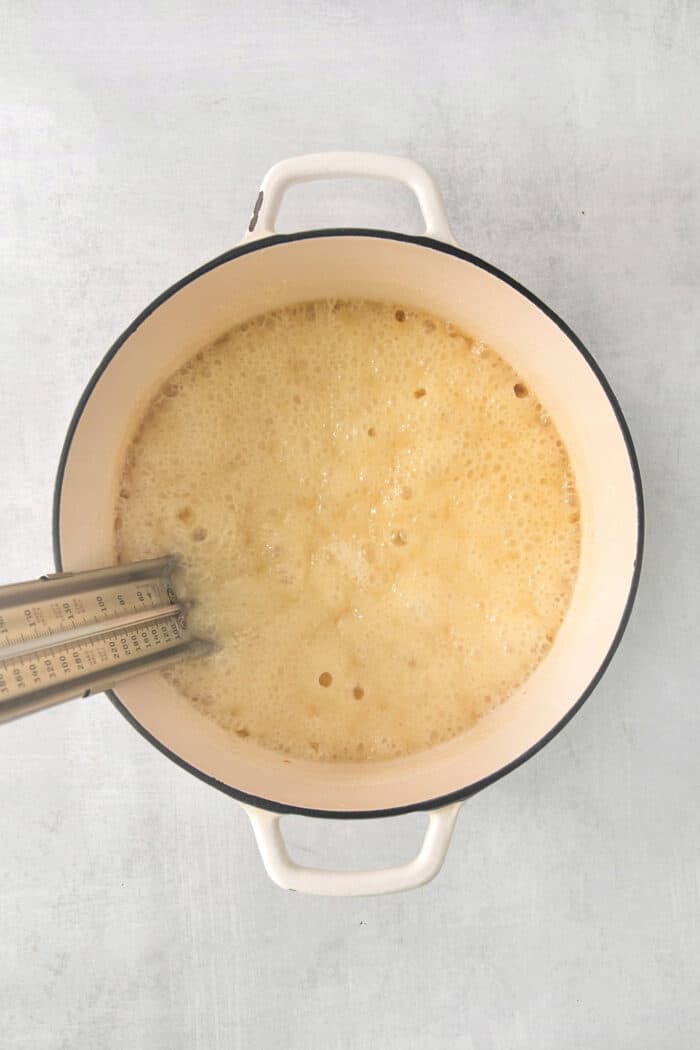 Fantasy Fudge is a thick, rich, no-fail chocolatey fudge made with semi-sweet chocolate, marshmallow creme, and walnuts. A top down shot of a candy thermometer placed in a pot of fudge.