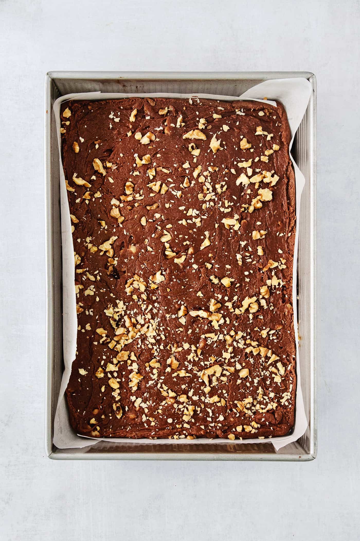 Fantasy Fudge is a thick, rich, no-fail chocolatey fudge made with semi-sweet chocolate, marshmallow creme, and walnuts. A parchment-lined ray of Fantasy Fudge as it cool.