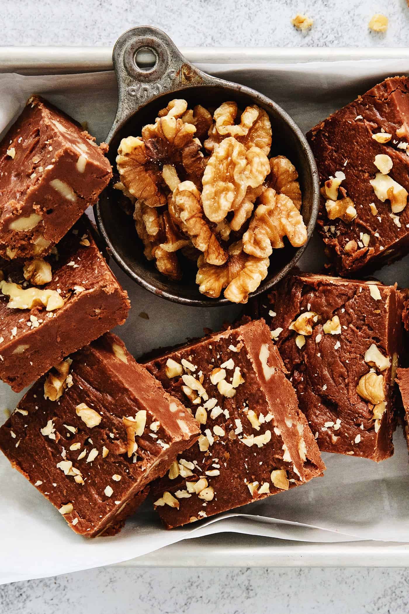 Fantasy Fudge is a thick, rich, no-fail chocolatey fudge made with semi-sweet chocolate, marshmallow creme, and walnuts. A tray of Fantasy Fudge is shown with walnuts above it.