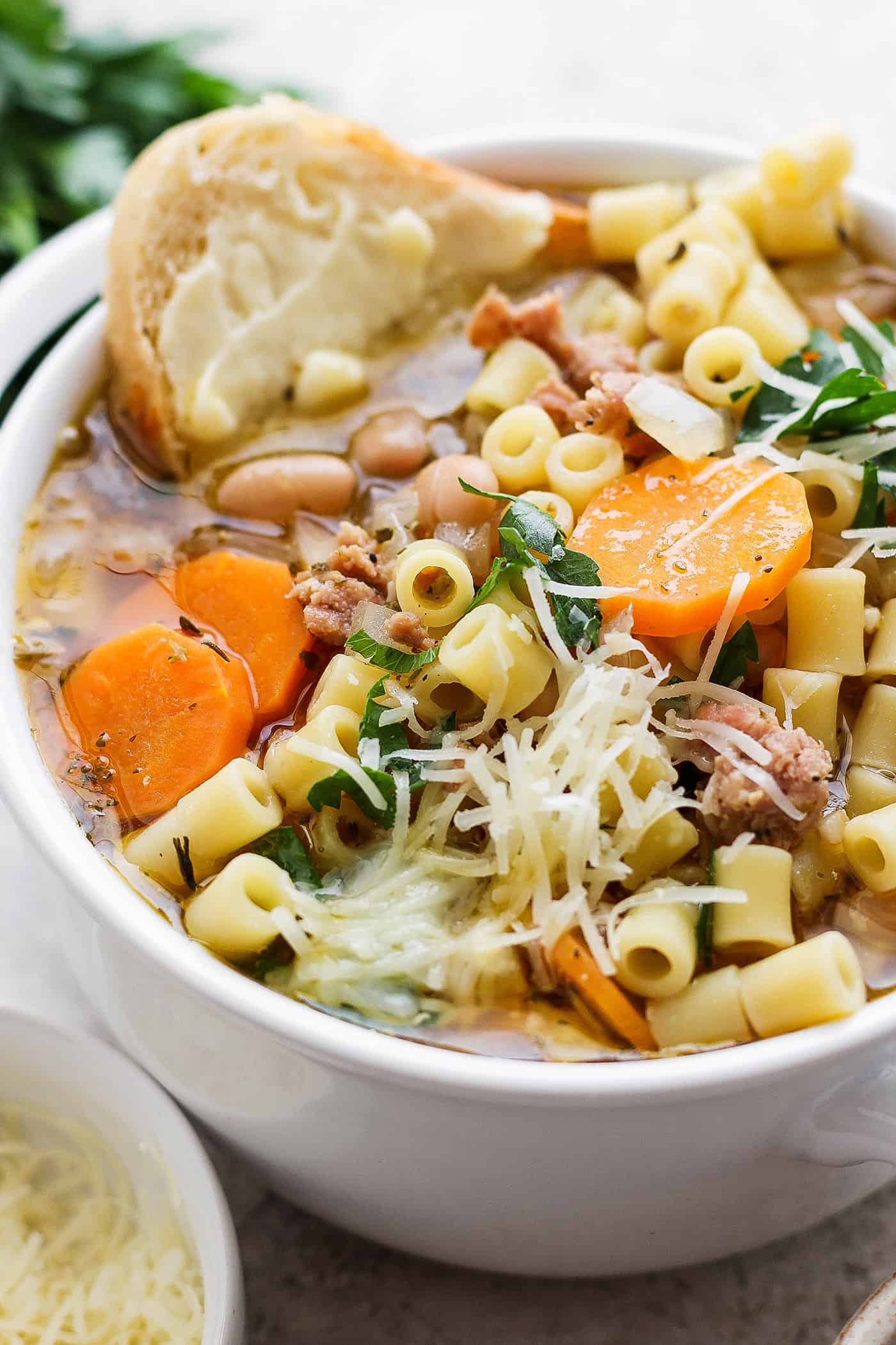 This Italian Sausage Soup recipe is packed with lots of Italian-flavored chicken sausage, creamy white beans, and big slices of carrot. A bowl of Italian sausage soup with a slice of bread and cheese on the side.
