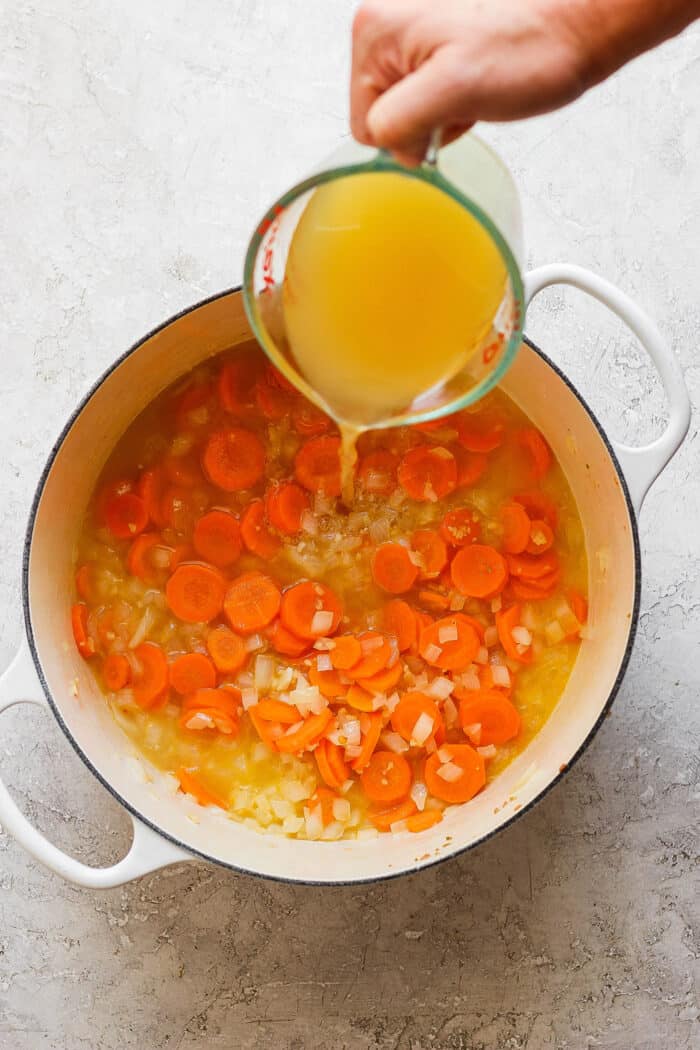 This Italian Sausage Soup recipe is packed with lots of Italian-flavored chicken sausage, creamy white beans, and big slices of carrot. Broth is poured from a measuring cup into a pot with carrot coins.