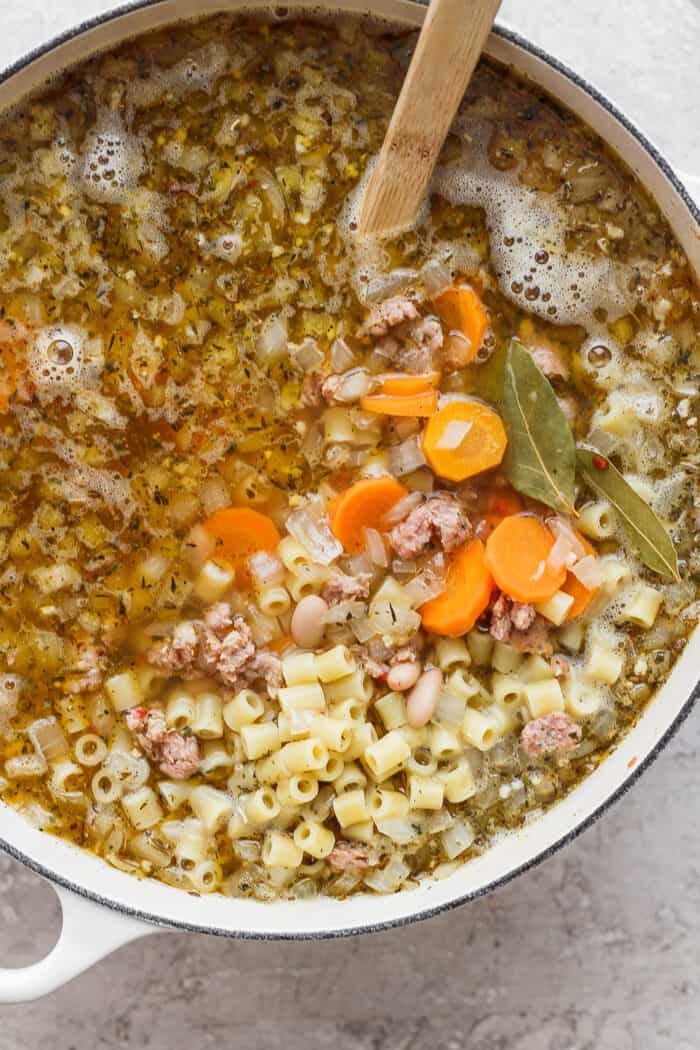 This Italian Sausage Soup recipe is packed with lots of Italian-flavored chicken sausage, creamy white beans, and big slices of carrot. A close up shot shows a pot of Italian sausage soup with carrot coins and pasta.
