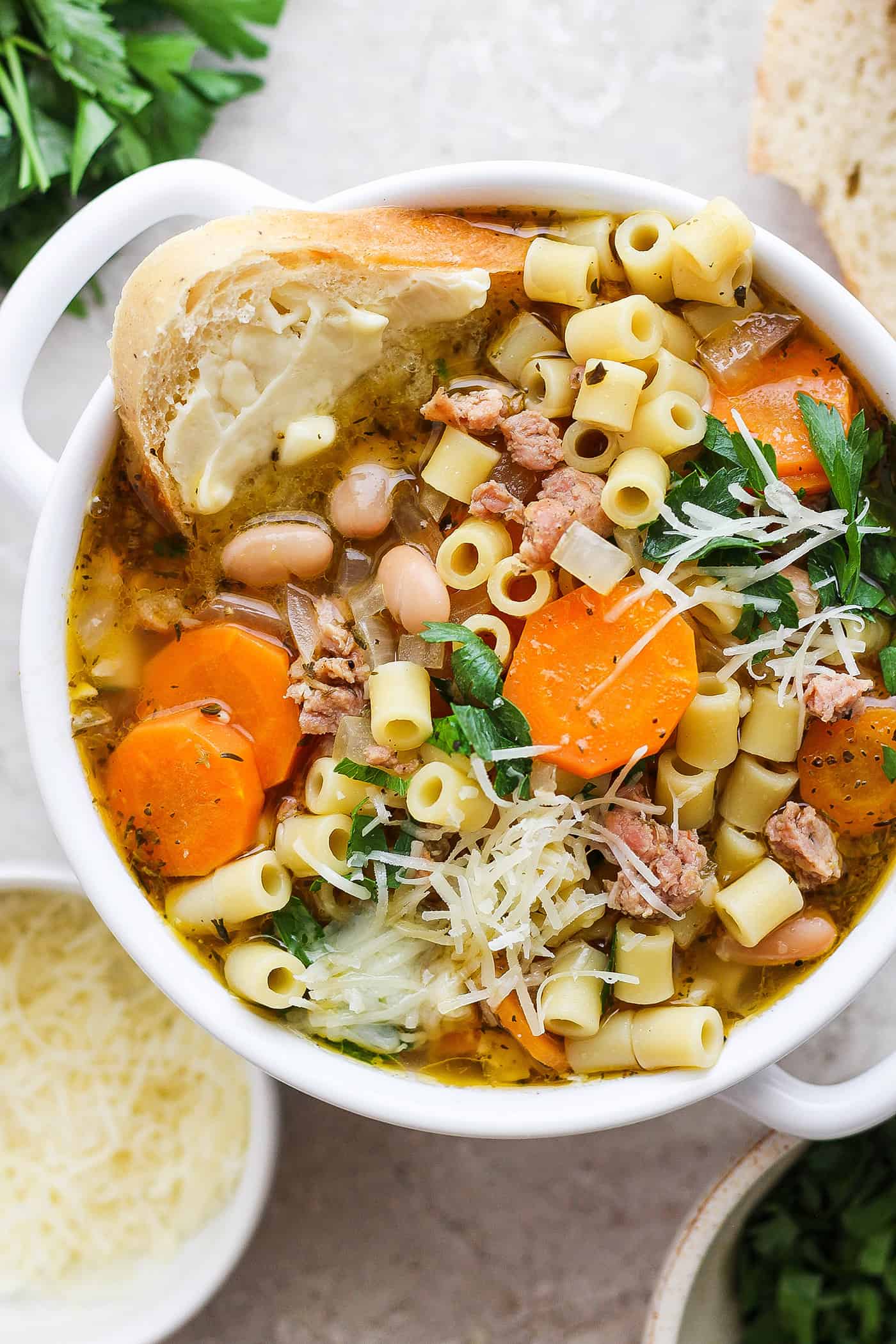 This Italian Sausage Soup recipe is packed with lots of Italian-flavored chicken sausage, creamy white beans, and big slices of carrot. A bowl of Italian sausage soup with a slice of bread and cheese on the side.