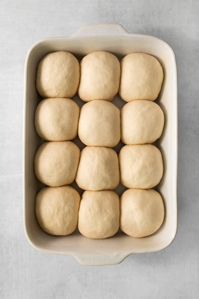 These copycat Rhodes Rolls are light and fluffy with a tender crumb and delicate flavor. Perfect for holiday meals! Rolls of proofed dough are shown in a pan to make rhodes rolls.