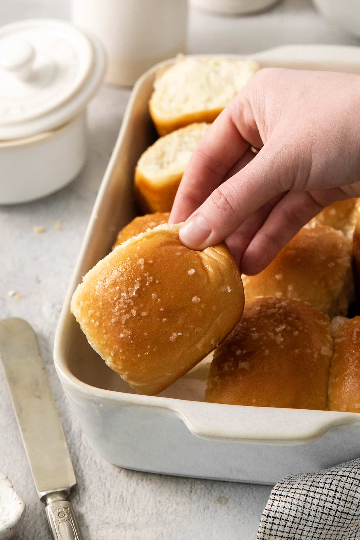 These copycat Rhodes Rolls are light and fluffy with a tender crumb and delicate flavor. Perfect for holiday meals! A hand lifts out a rhodes roll from a pan of rolls.