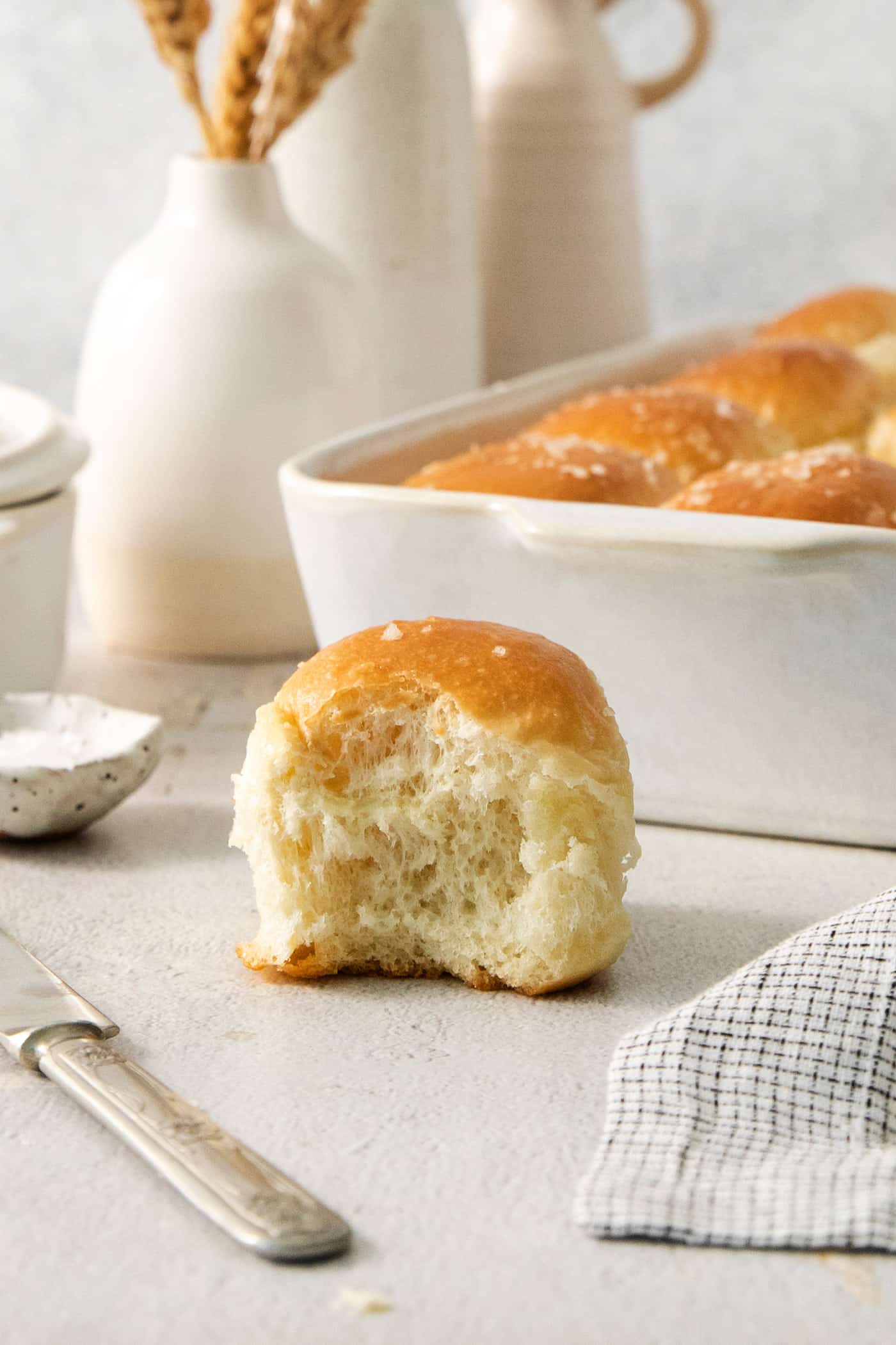 These copycat Rhodes Rolls are light and fluffy with a tender crumb and delicate flavor. Perfect for holiday meals! A rhodes roll is shown in front of a pan of rolls.