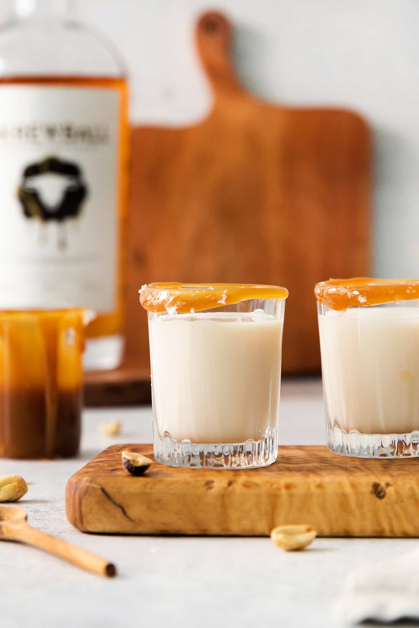 This Salted Nut Roll Shot is a fantastic twist on the salted nut roll candy bar with Rumchata, peanut butter whiskey, and vanilla vodka. Two salted nut roll shot drinks are shown on a cutting board.