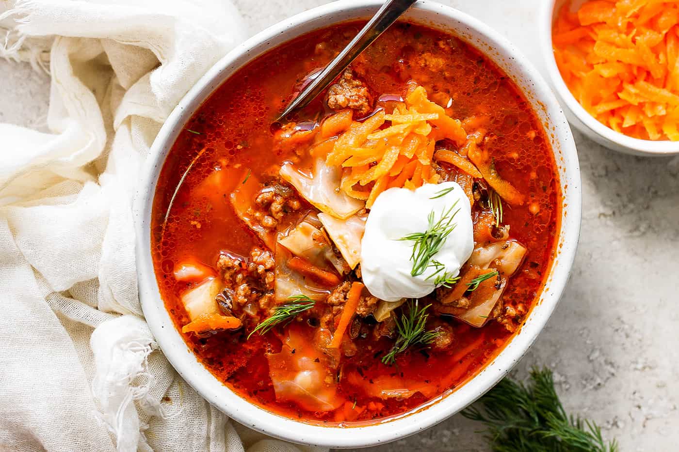 A bowl of unstuffed cabbage roll soup topped with carrot garnish and sour cream.