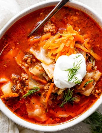 A bowl of unstuffed cabbage roll soup topped with carrot garnish and sour cream.