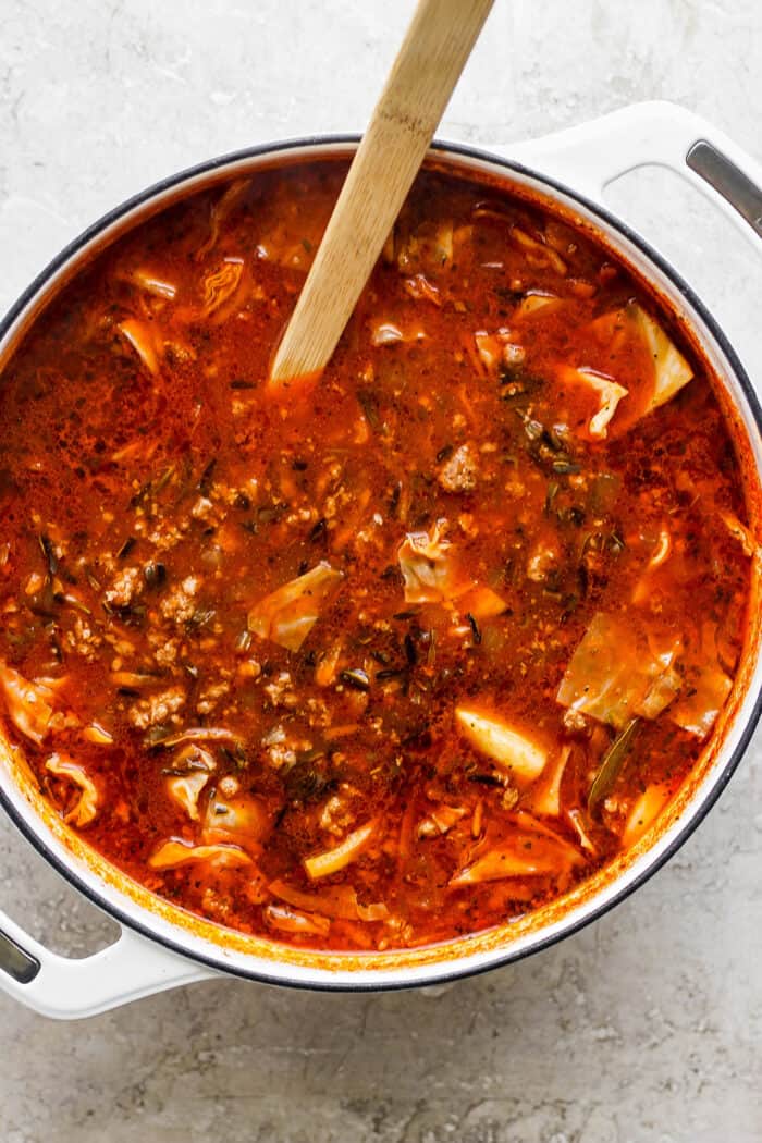 A wooden spoon stirs a pot of unstuffed cabbage roll soup.
