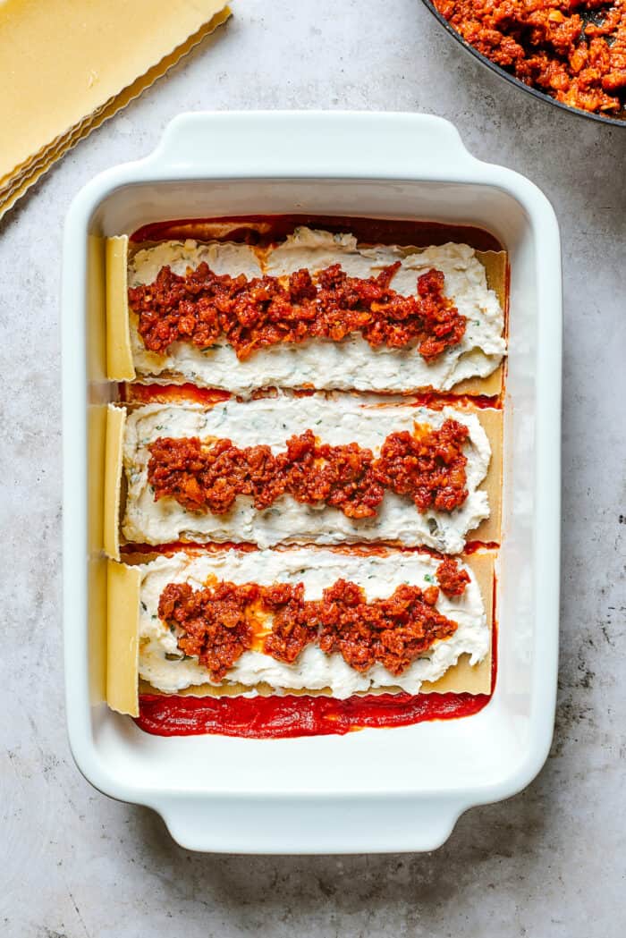 These cheesy Lasagna Roll Ups include a hearty blend of cheeses and sausage-flecked meat sauce that's wrapped in tender noodles. A closer up shot of layers of lasagna pasta topped with cheese filling and meat sauce.