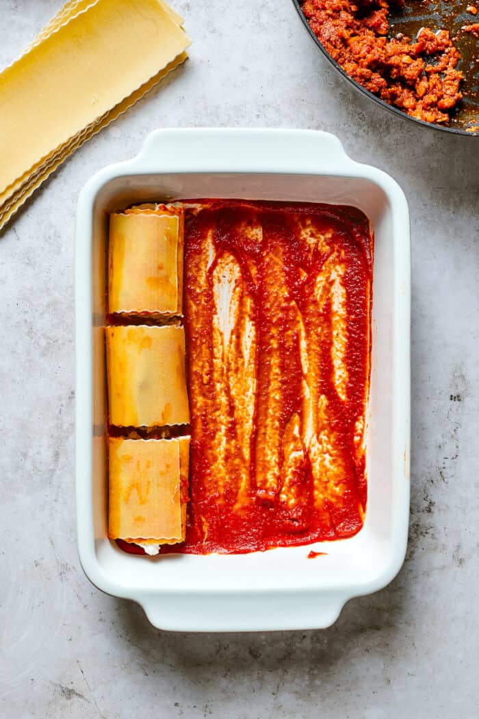 These cheesy Lasagna Roll Ups include a hearty blend of cheeses and sausage-flecked meat sauce that's wrapped in tender noodles. Three lasagna roll ups are shown on top of red sauce in a white baking dish.