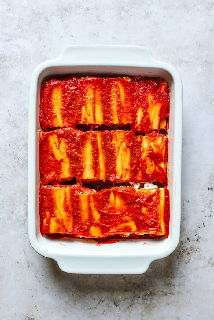 These cheesy Lasagna Roll Ups include a hearty blend of cheeses and sausage-flecked meat sauce that's wrapped in tender noodles. Lasagna roll ups are shown topped with red sauce in a white baking dish.