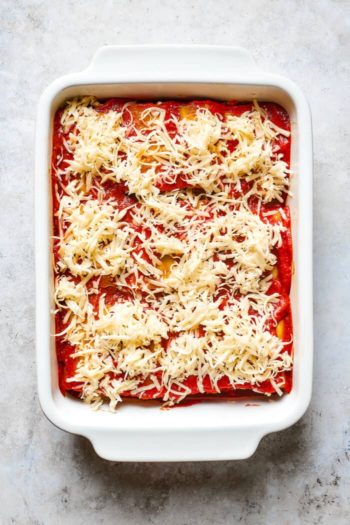 These cheesy Lasagna Roll Ups include a hearty blend of cheeses and sausage-flecked meat sauce that's wrapped in tender noodles. Shredded mozzarella cheese is scattered on top of a baking dish of lasagna roll ups.