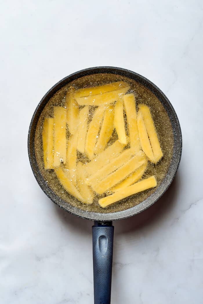 This Salchipapa recipe features crispy homemade french fries scattered with slices of beef hot dogs for a quick meal. Sliced potatoes fry in oil in a frying pan.