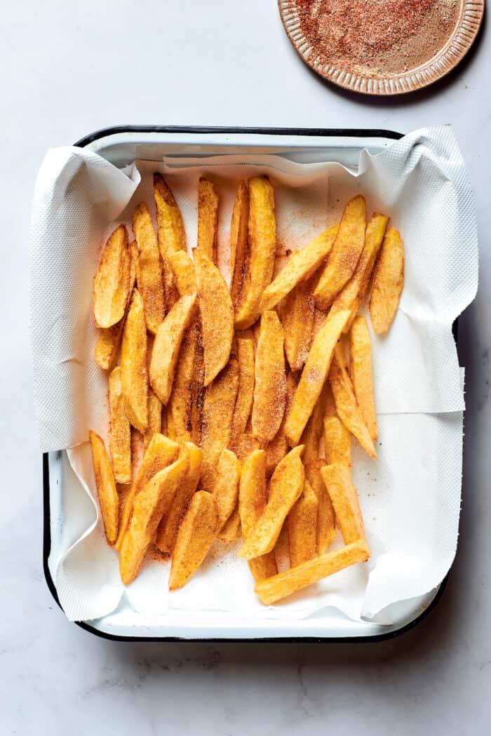 This Salchipapa recipe features crispy homemade french fries scattered with slices of beef hot dogs for a quick meal. French fried potatoes drain on a paper towel-lined pan.