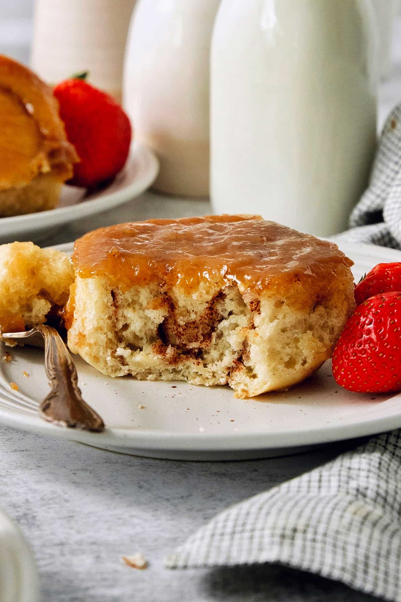 Sweet and pillowy Caramel Rolls make any morning special! Yeast dough and homemade caramel sauce make the ultimate breakfast treat. A caramel roll on a white plate with a piece cut out, a fork to its left, and strawberries to the right.