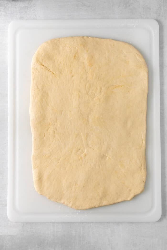 Sweet and pillowy Caramel Rolls make any morning special! Yeast dough and homemade caramel sauce make the ultimate breakfast treat. A rectangle of caramel rolls dough is stretched out on a white cutting board.