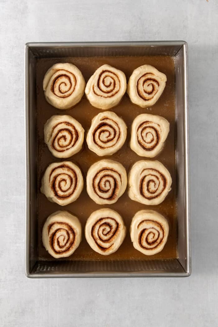 Sweet and pillowy Caramel Rolls make any morning special! Yeast dough and homemade caramel sauce make the ultimate breakfast treat. Twelve cut caramel rolls are shown on top of caramel sauce in a baking pan.