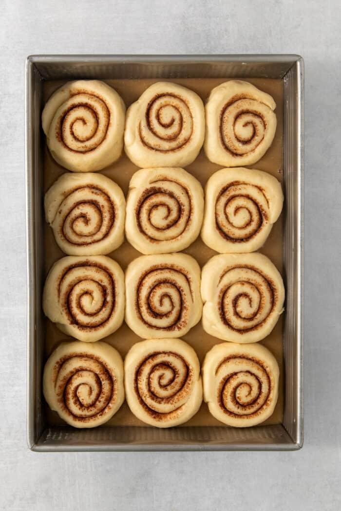Sweet and pillowy Caramel Rolls make any morning special! Yeast dough and homemade caramel sauce make the ultimate breakfast treat. Twelve proofed caramel rolls in a baking pan before being baked.