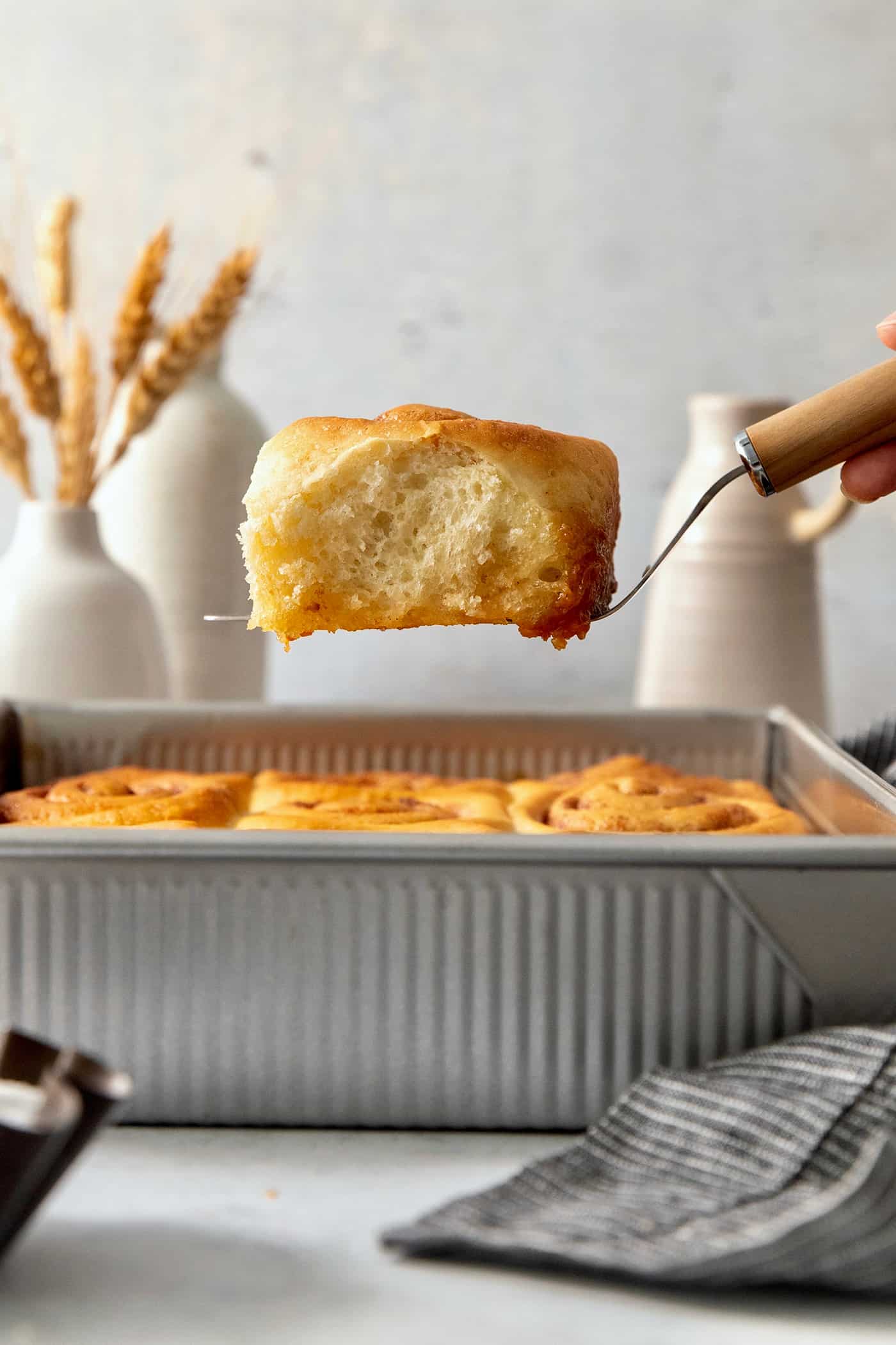 Sweet and pillowy Caramel Rolls make any morning special! Yeast dough and homemade caramel sauce make the ultimate breakfast treat. A hand holding a spatula lifts out one fluffy baked caramel roll from a metal baking pan of rolls.
