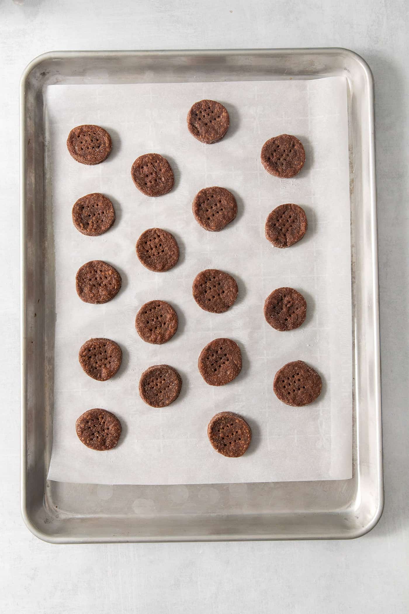 Chocolate wafer cookie rounds are spread out on a parchment paper lined cookie sheet and pricked with a fork.