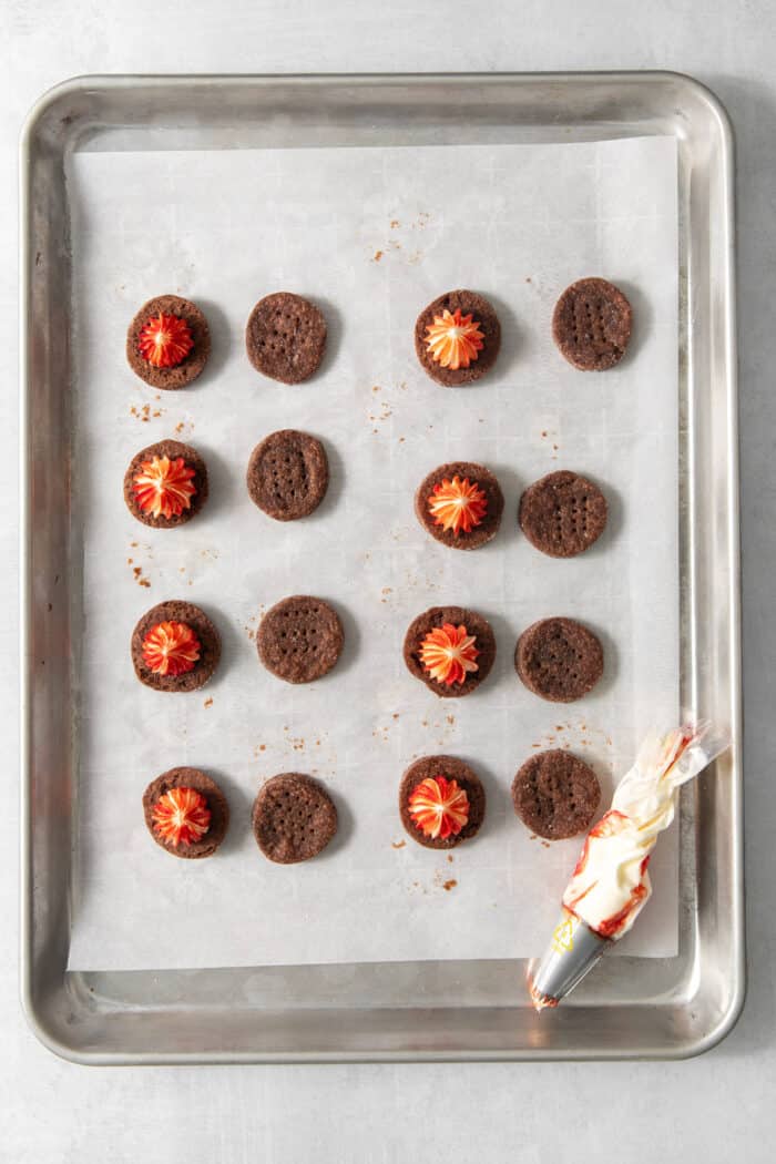 These Chocolate Cream Wafer Cookies feature buttery cocoa cookies that are soft, tender, and filled with a rich buttercream. Chocolate cream wafer cookies on a parchment paper lined baking sheet - half are topped with peppermint buttercream filling.