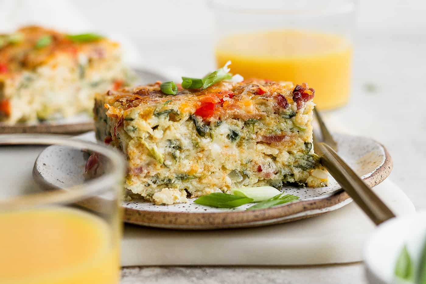 This protein-packed cottage cheese egg bake recipe combines creamy, fluffy eggs and cottage cheese with colorful veggies and crispy bacon. A plate of cottage cheese egg bake with a glass of orange juice.
