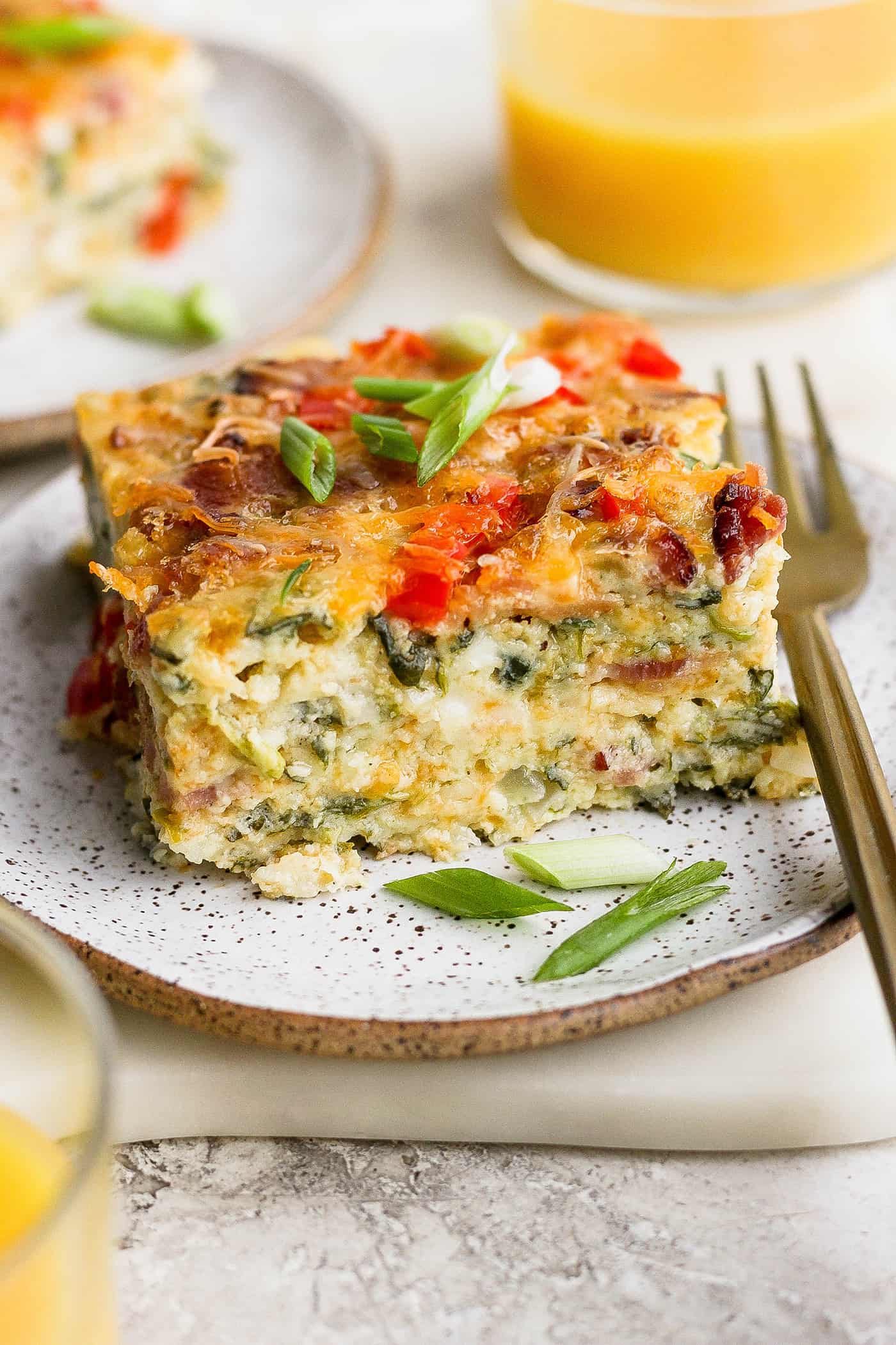 This protein-packed cottage cheese egg bake recipe combines creamy, fluffy eggs and cottage cheese with colorful veggies and crispy bacon. A plate of cottage cheese egg bake with a glass of orange juice.