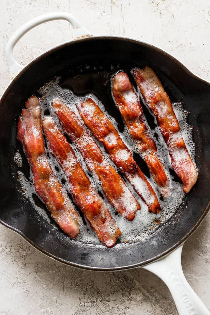 This protein-packed cottage cheese egg bake recipe combines creamy, fluffy eggs and cottage cheese with colorful veggies and crispy bacon. Strips of bacon cook in a cast iron skillet.