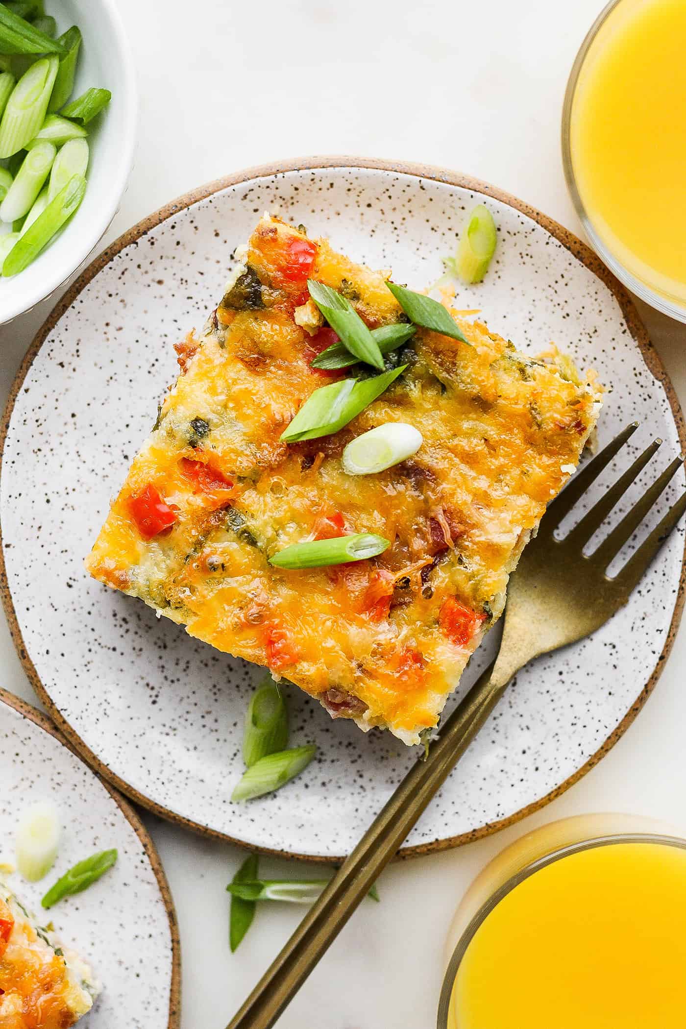 This protein-packed cottage cheese egg bake recipe combines creamy, fluffy eggs and cottage cheese with colorful veggies and crispy bacon. A top down shot of a piece of cottage cheese egg bake on a plate with a fork.