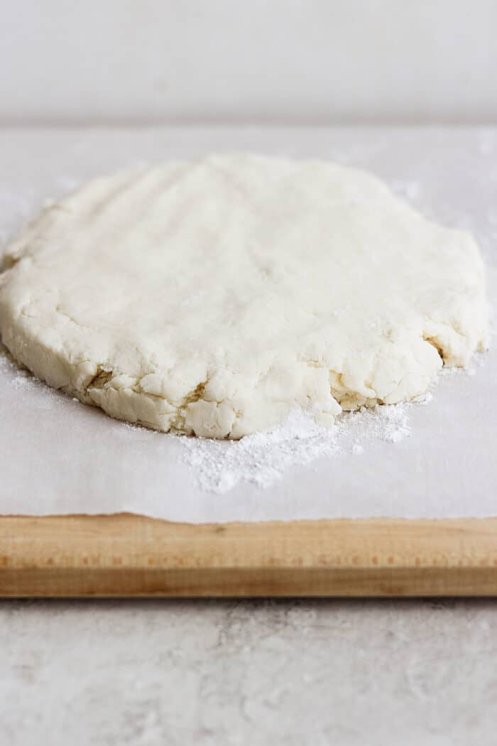 Rich, tender Cream Biscuits need just 3 simple ingredients and 15 minutes to make! Serve them with brunch or a hot bowl of homemade soup. A round of cream biscuit dough rests on a white piece of parchment paper on top of a wooden cutting board.