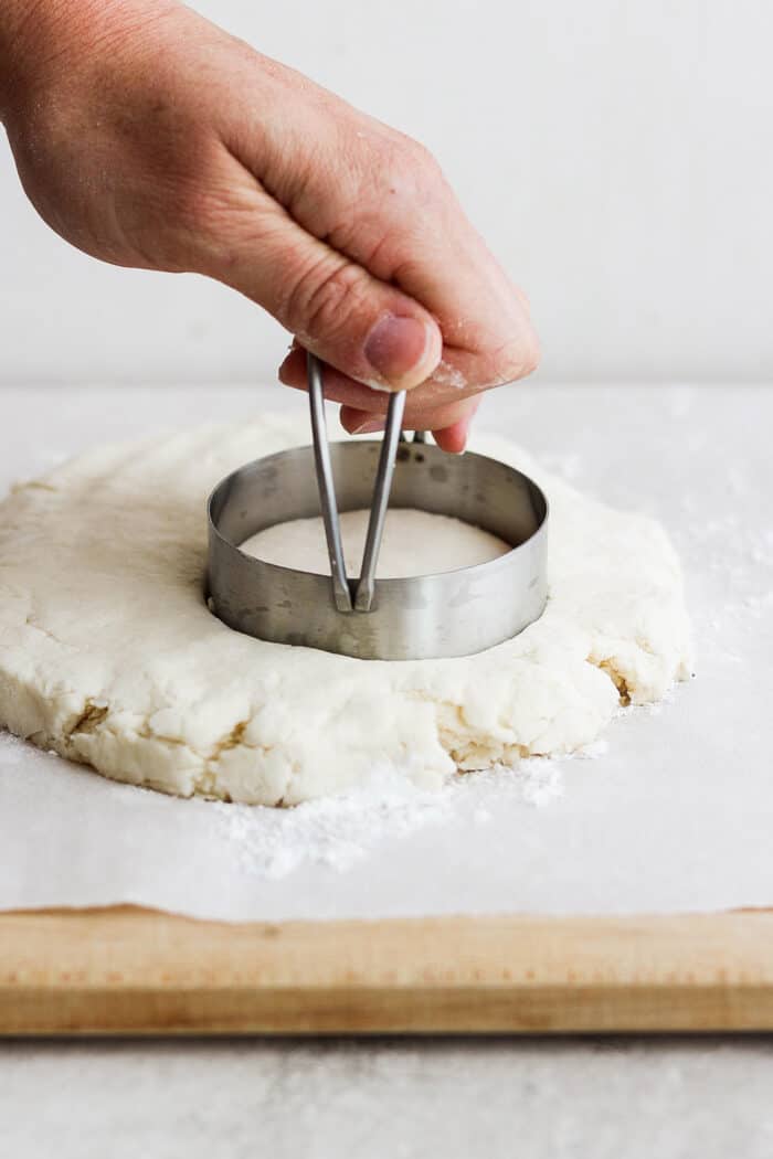 Rich, tender Cream Biscuits need just 3 simple ingredients and 15 minutes to make! Serve them with brunch or a hot bowl of homemade soup. A hand uses a metal biscuit cutter to cut out a cream biscuit from a piece of dough.