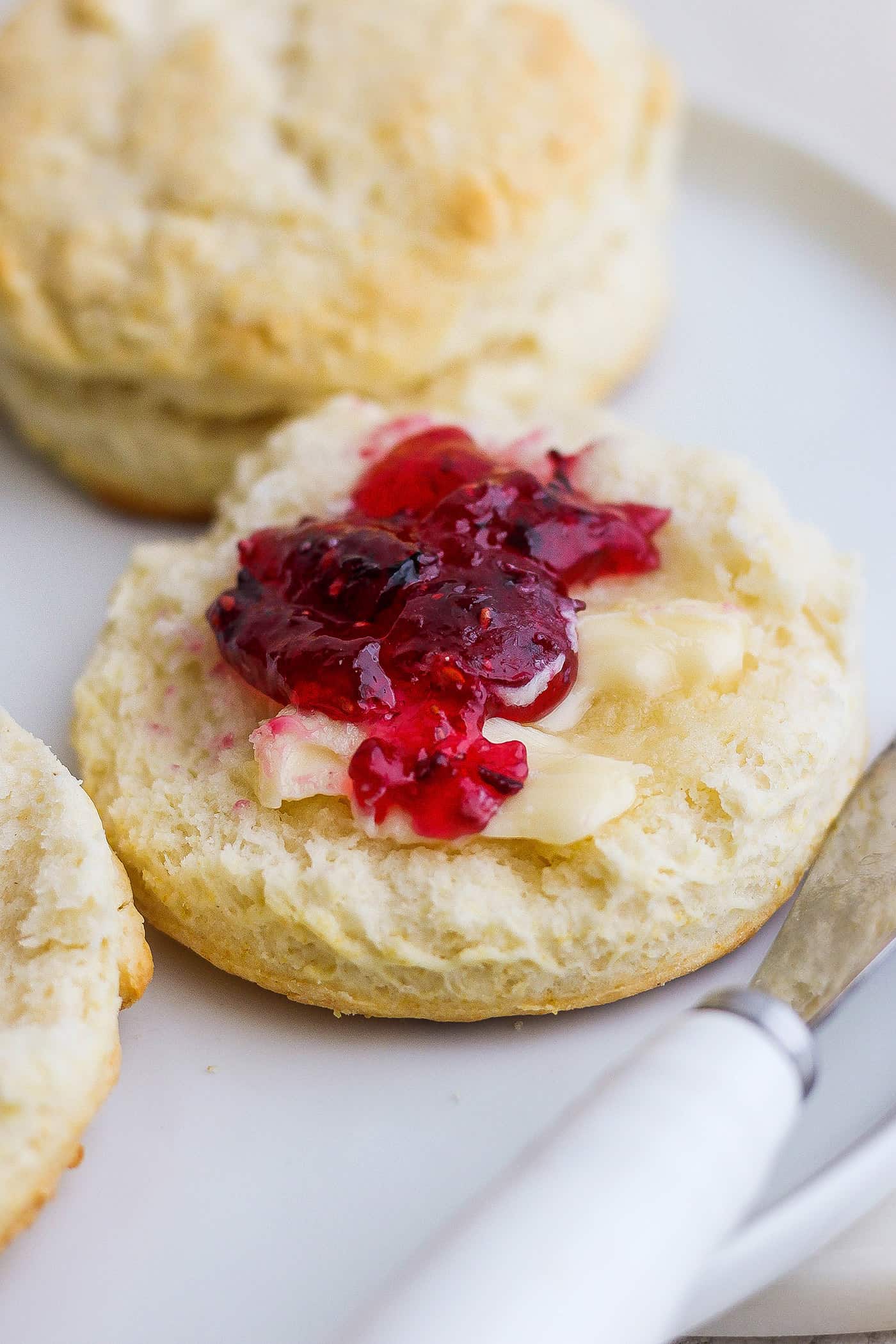 Rich, tender Cream Biscuits need just 3 simple ingredients and 15 minutes to make! Serve them with brunch or a hot bowl of homemade soup. A cut cream biscuit is shown spread with butter and jam with more biscuits in the background.