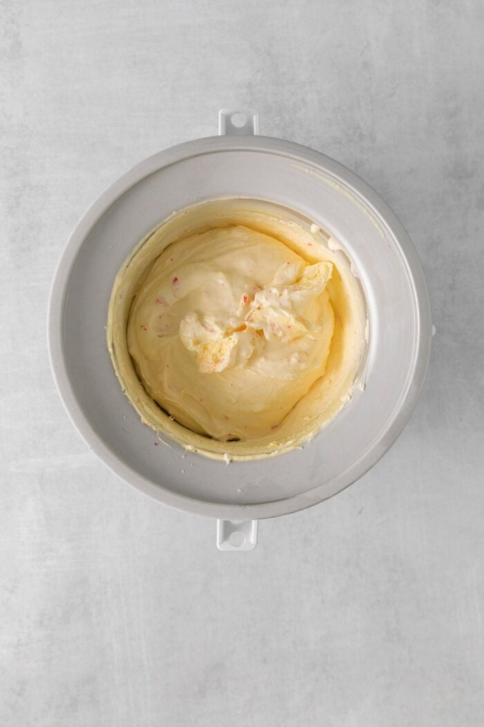 Creamy, dreamy Peppermint Ice Cream is so easy to make at home! Peppermint-infused ice cream is scattered with bits of candy canes. Churned ice cream base is shown in an ice cream maker after being churned to a soft consistency.