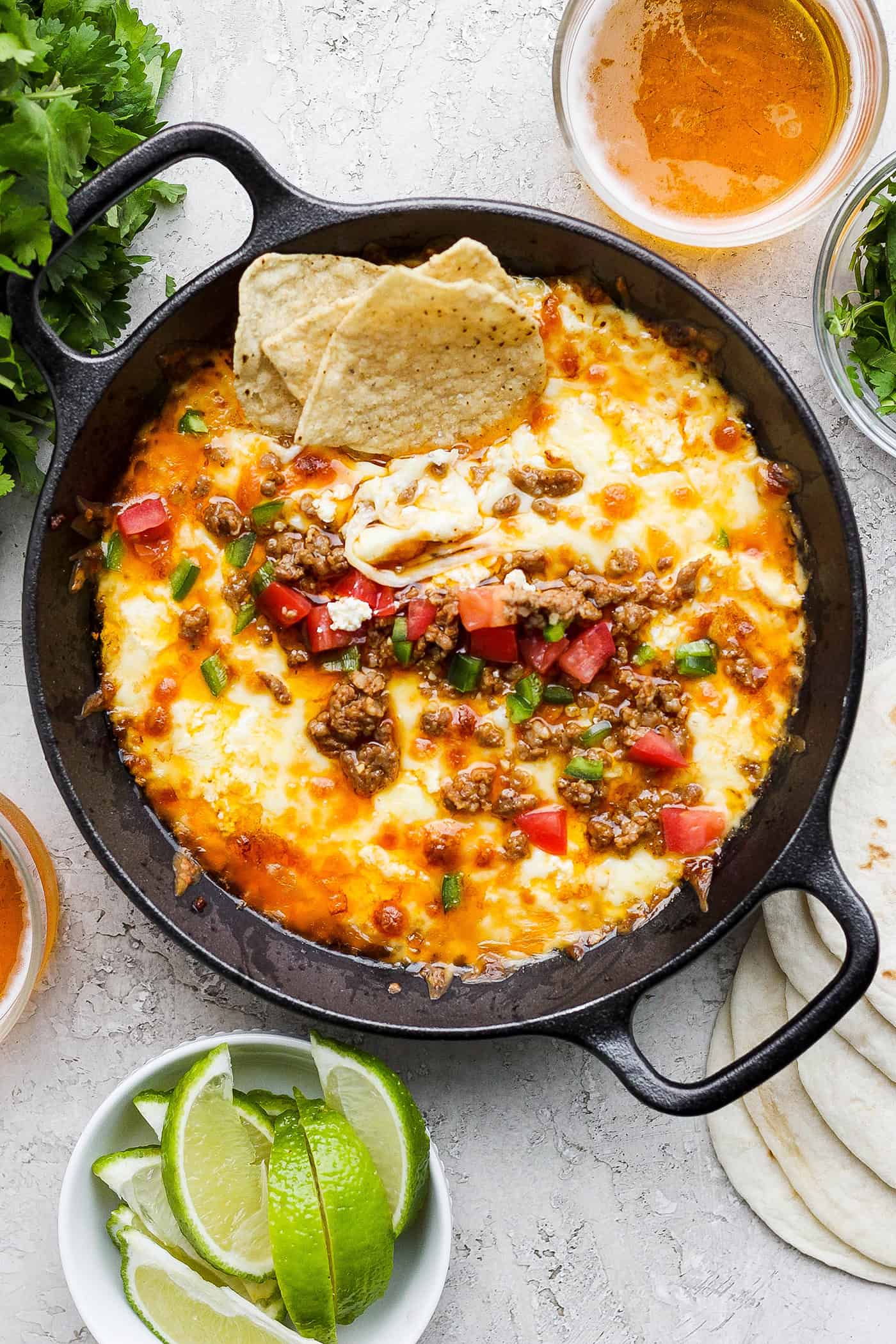 Creamy and just a little spicy, Queso Fundido is an easy, go-to dip! Melted cheese and chorizo are topped with fresh tomatoes and jalapeno. A black cast iron skillet of queso fundido topped with chorizo, tomatoes, and jalapeno and garnished with tortilla chips, with lime wedges on the side.
