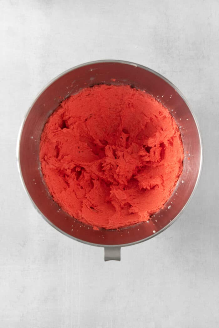 These Red Velvet Cookies are soft and chewy, with a crisp sugar coating and a hint of cocoa and vanilla for flavor. Red food coloring is adding to butter and sugar in a metal bowl.