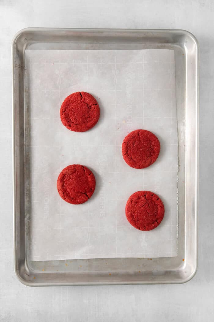 These Red Velvet Cookies are soft and chewy, with a crisp sugar coating and a hint of cocoa and vanilla for flavor. Four red velvet cookies on a baking sheet.
