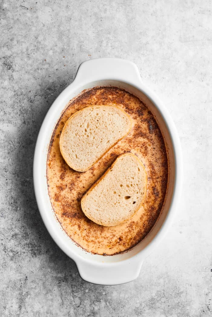 Bananas Foster French Toast features rich and tender slices of egg-soaked sweet bread that are topped with rum-spiked caramelized bananas. Two slices of bread are dipped in French toast batter in an oval baking dish.