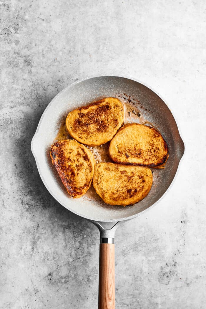 Bananas Foster French Toast features rich and tender slices of egg-soaked sweet bread that are topped with rum-spiked caramelized bananas. Four pieces of bananas foster French toast cook in a skillet.