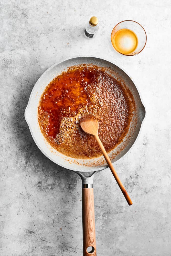 Bananas Foster French Toast features rich and tender slices of egg-soaked sweet bread that are topped with rum-spiked caramelized bananas. Ground spices are stirred into a skillet of melted butter with a wooded spoon.