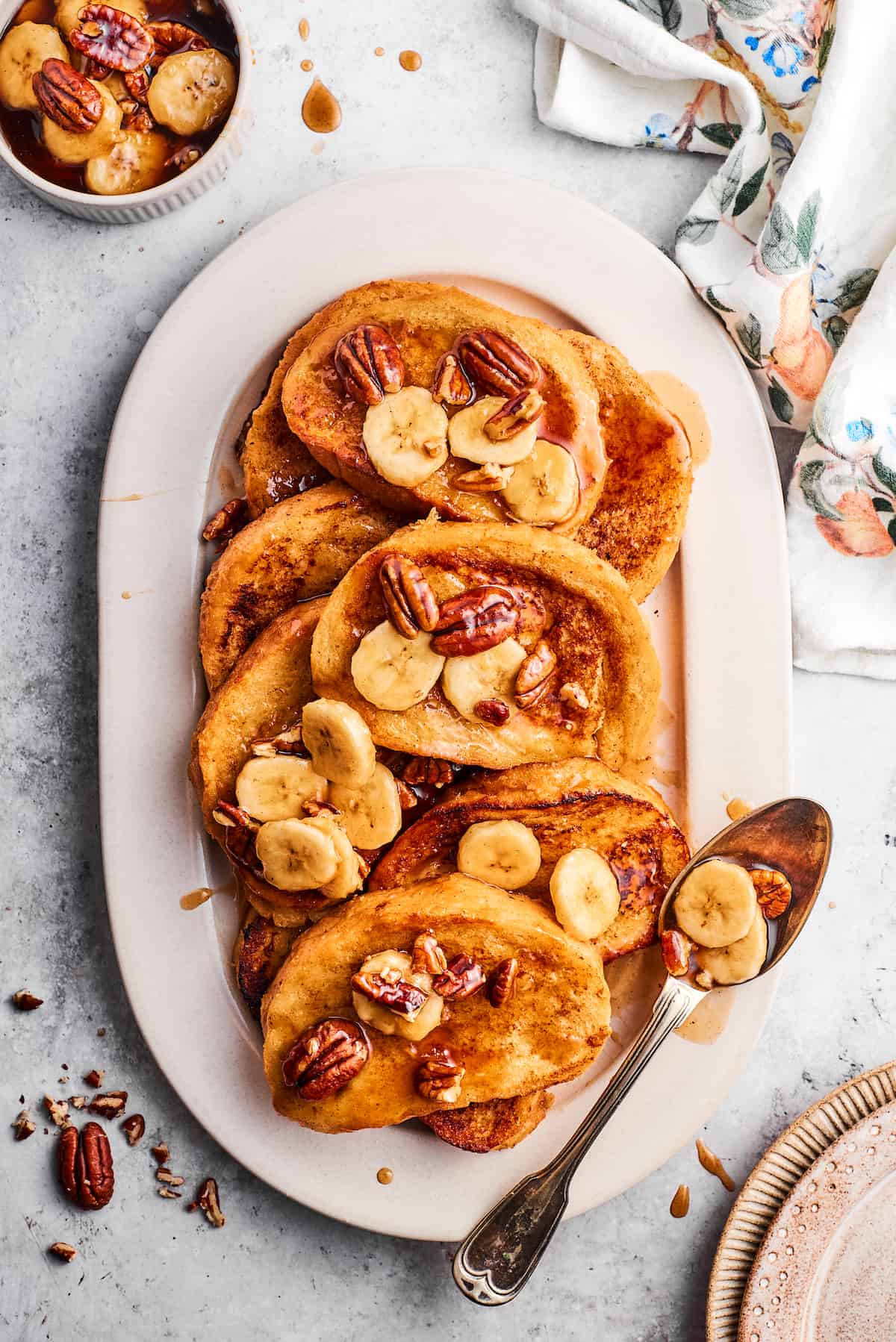 An oval serving dish holds slices of bananas foster French toast topped with bananas.
