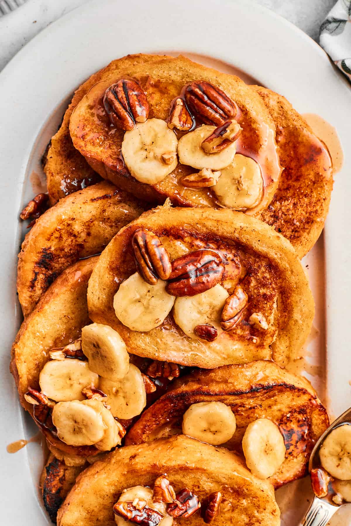 Bananas Foster French Toast features rich and tender slices of egg-soaked sweet bread that are topped with rum-spiked caramelized bananas. Slices of bananas foster French toast are piled on a serving platter.