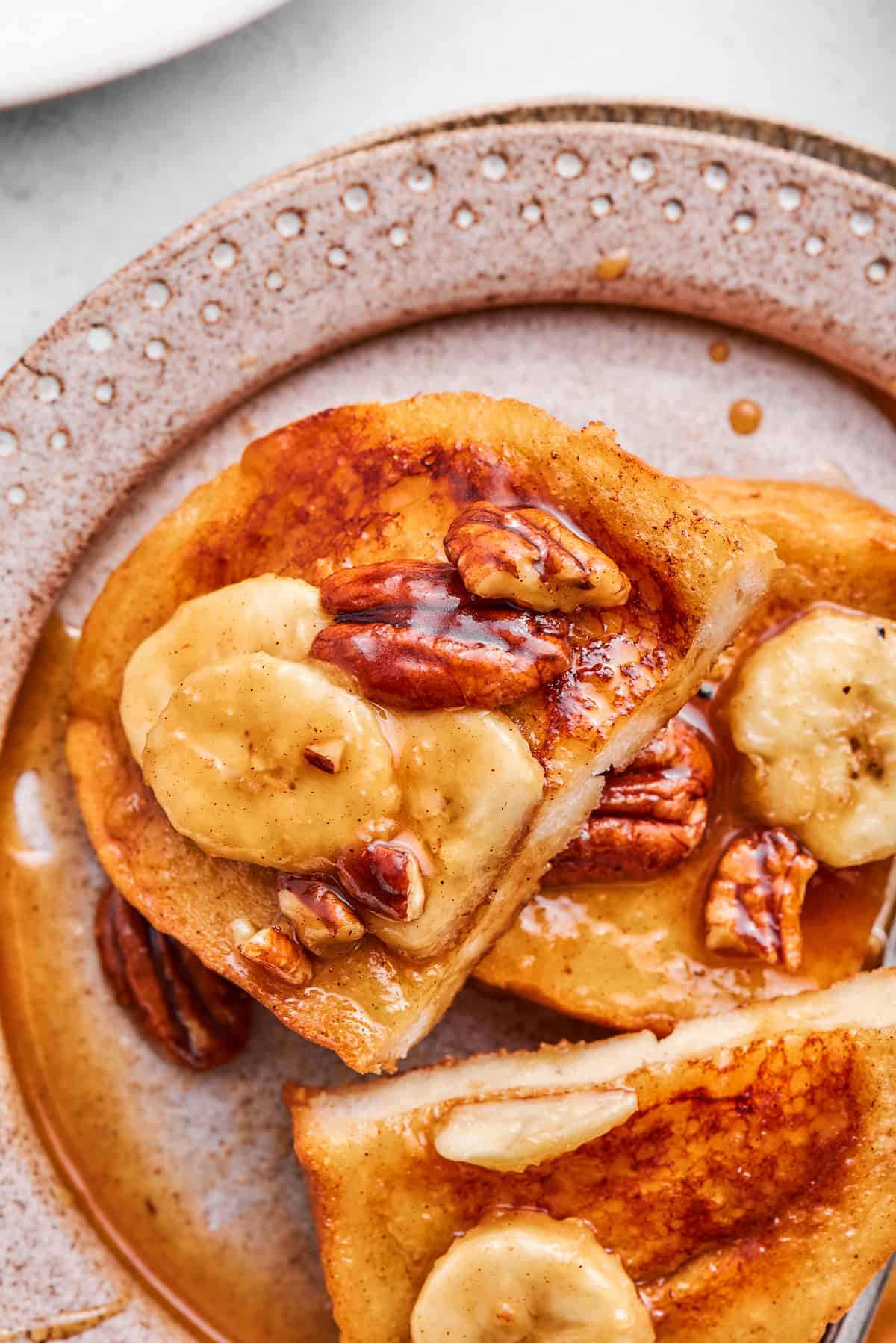 Bananas Foster French Toast features rich and tender slices of egg-soaked sweet bread that are topped with rum-spiked caramelized bananas. Several slices of bananas foster French toast are shown on a plate.