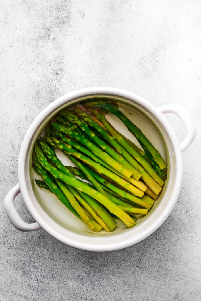 Creamy Chicken Madeira pairs tender chicken breasts with bright asparagus in a rich sauce. Add savory sautéed mushrooms and sweet wine. Asparagus spears blanch in a white pot.