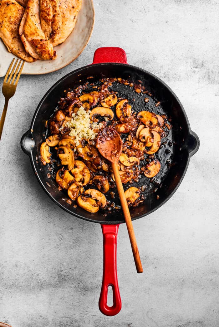 Creamy Chicken Madeira pairs tender chicken breasts with bright asparagus in a rich sauce. Add savory sautéed mushrooms and sweet wine. Garlic is added to the skillet of mushrooms.