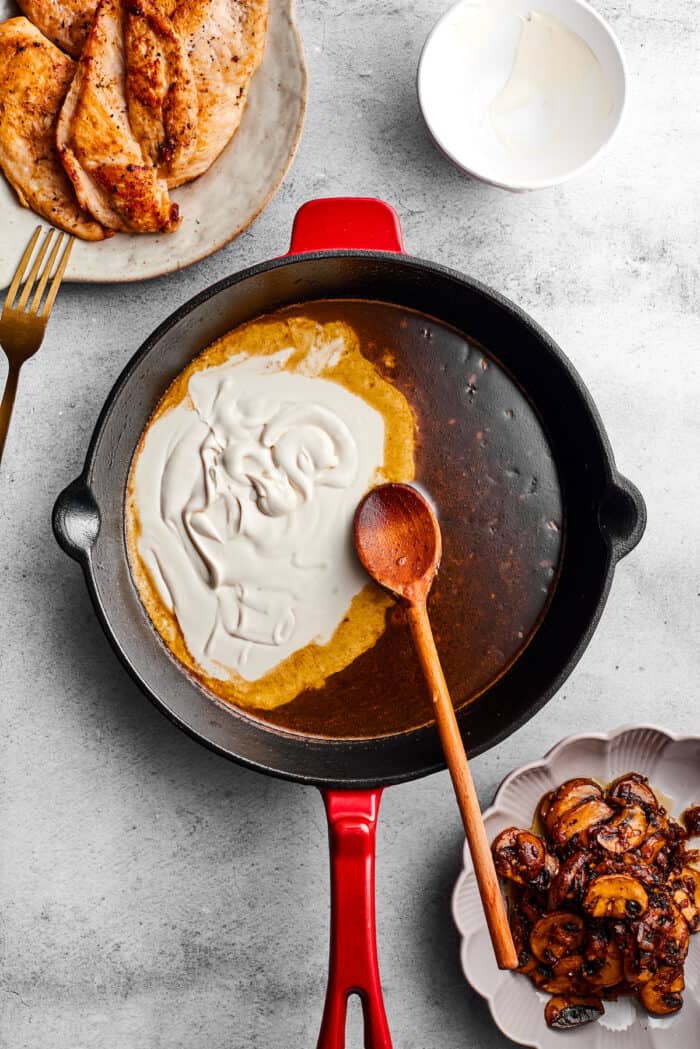 Creamy Chicken Madeira pairs tender chicken breasts with bright asparagus in a rich sauce. Add savory sautéed mushrooms and sweet wine. A wooden spoon stirs cream into a skillet to make sauce for chicken madeira.